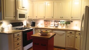 Una cocina con gabinetes blancos, estufa, horno, microondas e isla roja con un bol de fruta.