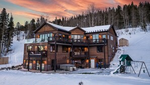 Une cabane en bois à plusieurs étages, dotée de balcons, d’un porche couvert et surplombant un paysage enneigé.