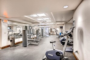 Ein Fitnessstudio mit verschiedenen Trainingsgeräten, einer Spiegelwand und einem Ausgangsschild.