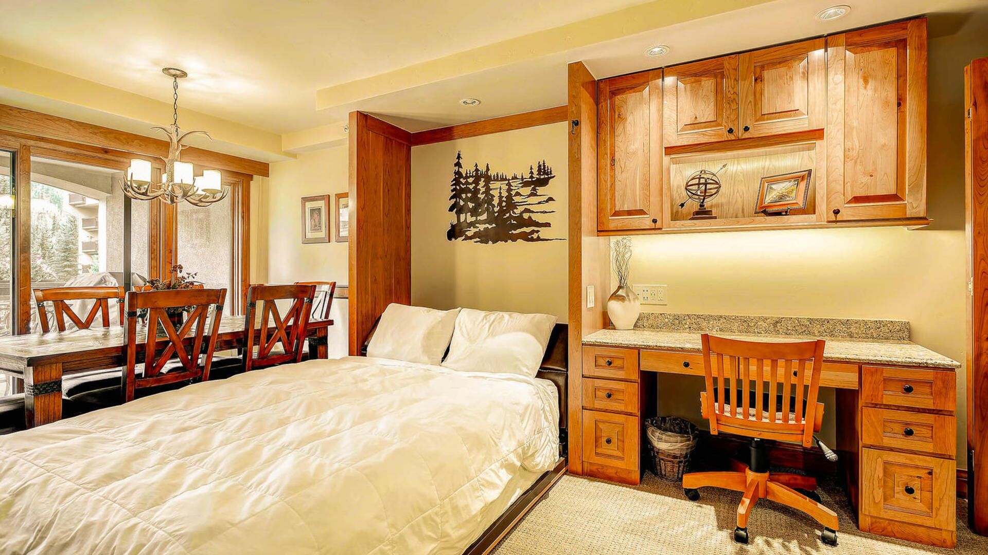 Un dormitorio con una cama, un escritorio y una silla. Se ve una ventana con vistas a árboles.