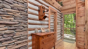 Ein Holzblockhaus-Interieur mit Steinwand, Holzkommode, Spiegel und einer Tür, die auf einen Balkon führt.