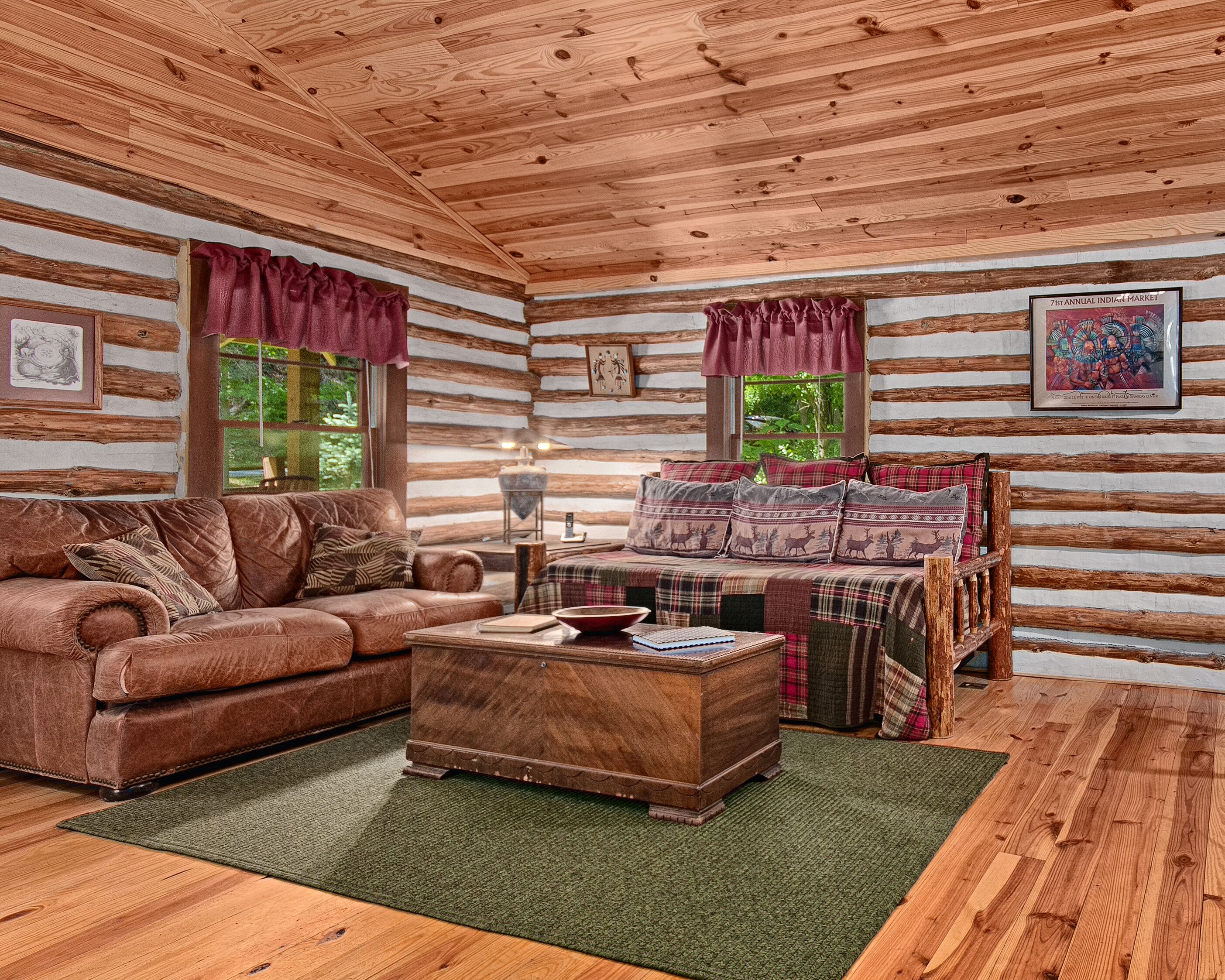 L’intérieur d’une cabane en rondins, avec un canapé en cuir, une table basse en bois, une literie à carreaux et un tableau encadré accroché au mur.