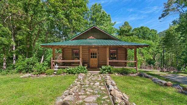 Ein rustikales Holzhaus mit grüner Dachdeckung, einem Steinweg, der zum Eingang führt, und einem Wald im Hintergrund.