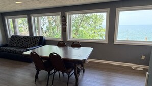 A dining area with a large table and chairs, a sofa, and large windows with a view of the sea. - Lake Access Retreat  Pet Friendly  Fire Pit (Geneva)