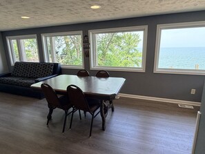 A dining area with a large table and chairs, a sofa, and large windows with a view of the sea.