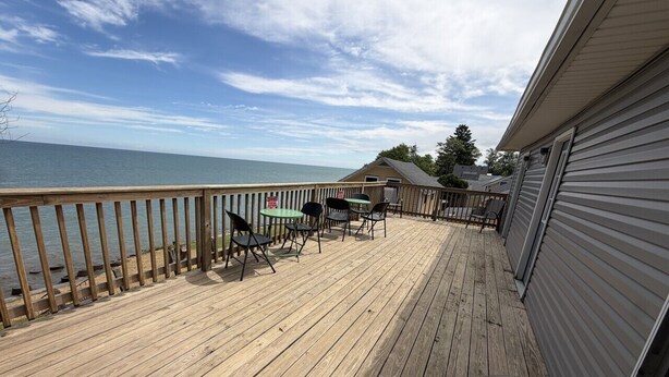 A wooden deck with outdoor furniture, a view of the water, and a building with a garage. - Lake Access Retreat  Pet Friendly  Fire Pit (Geneva)