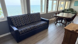 A room with a sofa, dining table, chairs, and large windows overlooking the sea. - Lake Access Retreat  Pet Friendly  Fire Pit (Geneva)