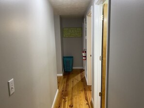 A narrow hallway with wooden flooring, a blue laundry basket, and a fire extinguisher on the wall. - Lake Access Retreat Pet Friendly Fire Pit (Geneva)