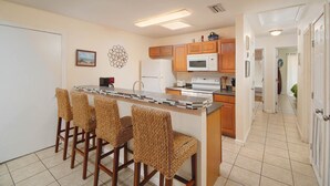 A kitchen with a central island, wooden chairs, a refrigerator, a microwave, and a stove.