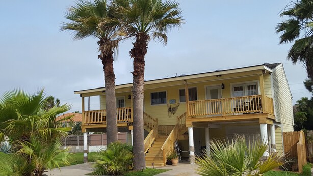 A two-story building with a balcony, palm trees, and a staircase leading to the upper floor.