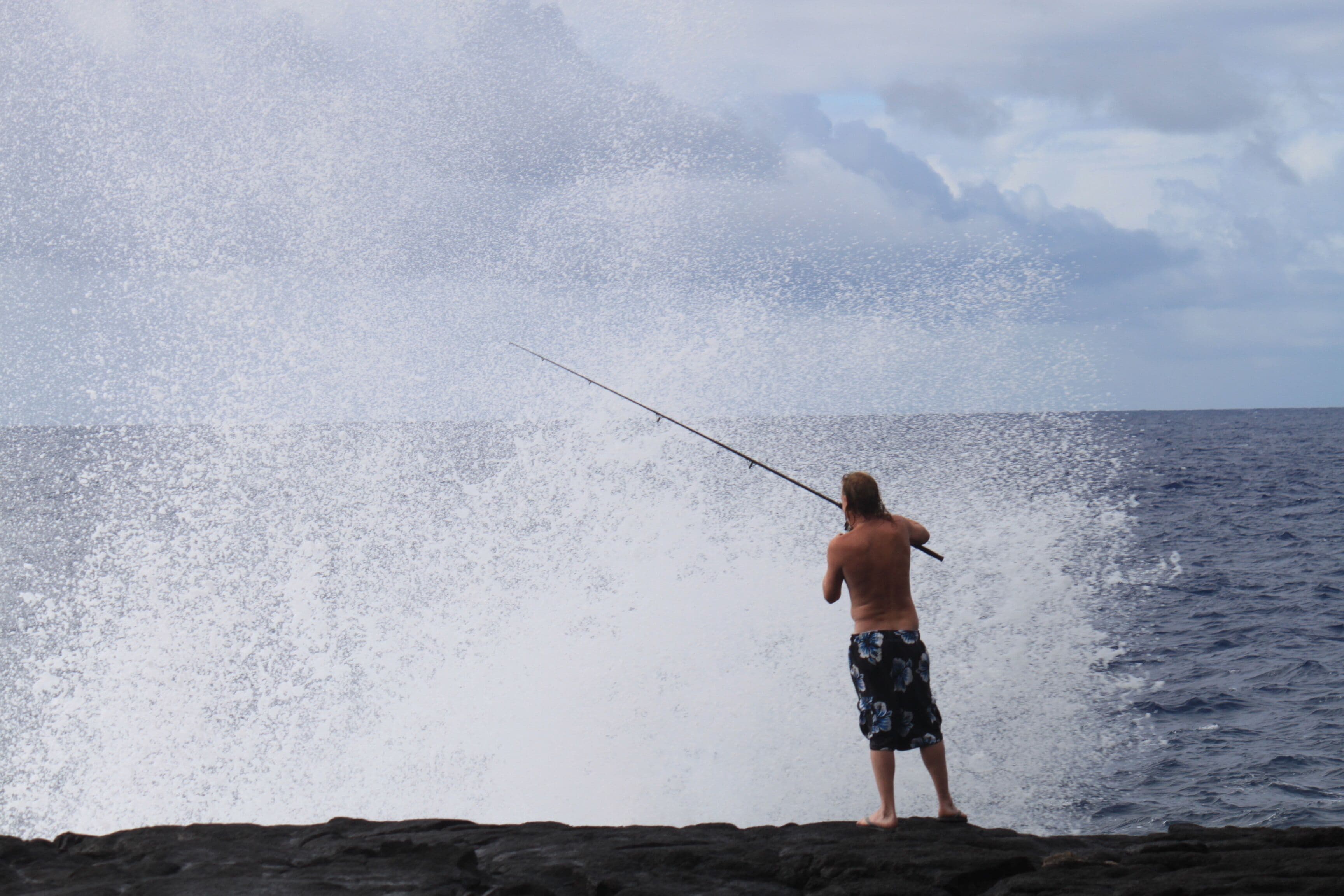 A person fishing on a rocky shore with the ocean in the background.