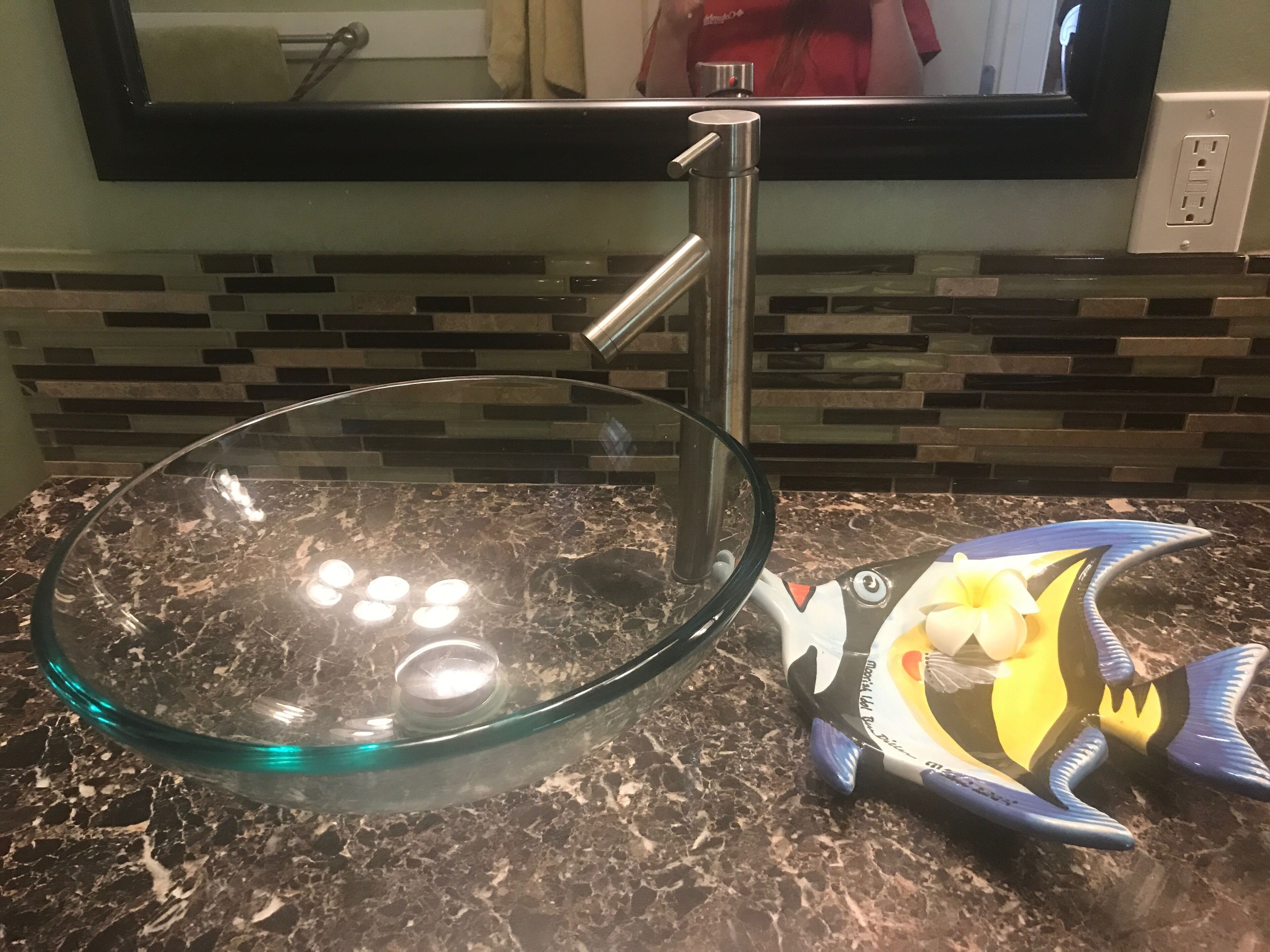 A glass bowl sink with a modern faucet, a decorative fish-shaped soap dispenser, and a tiled backsplash.