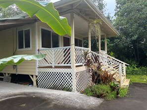 A house with a covered porch, a white lattice railing, and a large green leaf in the foreground.