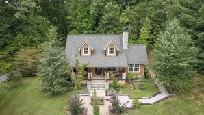 A two-story house with a stone chimney, a front porch, and a landscaped garden with a picnic table.