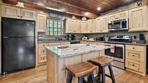 A kitchen with wooden cabinets, a black refrigerator, a microwave, an oven, and a granite countertop.