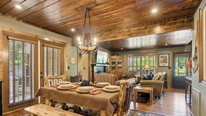 A rustic dining area with a wooden table and benches, a fireplace, and a cozy living room with a sofa and a television.