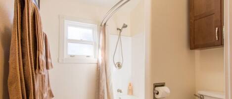 A bathroom with a white toilet, a shower, a towel rack with towels, and a small window.