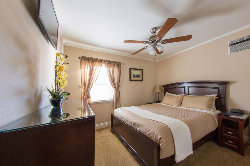 A bedroom with a bed, a ceiling fan, a nightstand, a dresser, and a window with curtains.