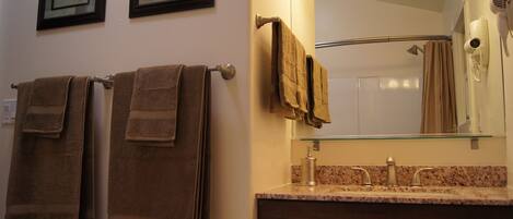 A bathroom with two towels hanging on a towel rack, a glass shelf above the sink, and a hairdryer on the wall.