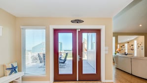 A room with a wooden floor, a bench with a starfish pillow, a door with a view to a balcony, and a beige wall. - Lei by the Sea, Beautiful 2nd Row Beach House with Elevator (Galveston)