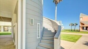 A corner of a building with a curved staircase leading to a landing. - Lei by the Sea, Beautiful 2nd Row Beach House with Elevator (Galveston)