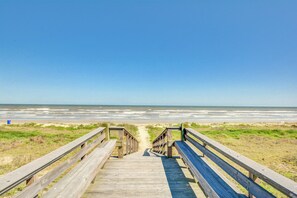 Une promenade en bois qui mène à une plage offrant une vue dégagée sur l’océan.