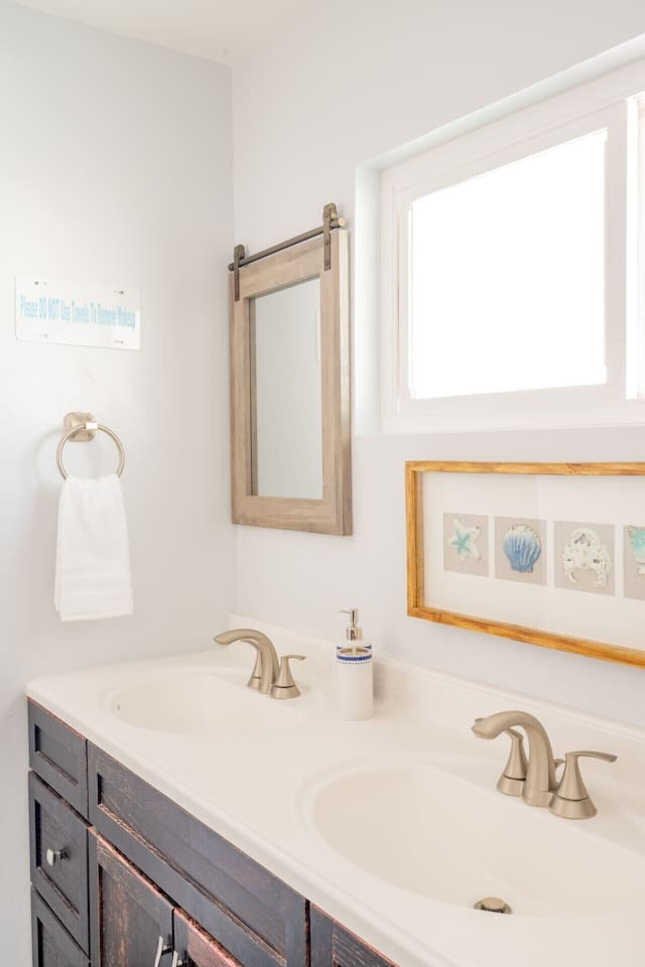 A bathroom with two sinks, a mirror, a towel ring, and a window.