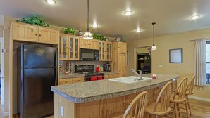 A kitchen with wooden cabinets, a black refrigerator, a granite countertop, and a bar area with wooden chairs. - Woodsy family getaway: private, hiking, wood stove, sleeps 12 (Parks)