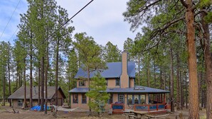 A two-story cabin with a covered porch, surrounded by tall pine trees. - Woodsy family getaway: private, hiking, wood stove, sleeps 12 (Parks)