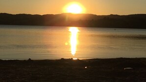 Un coucher de soleil sur un lac paisible, avec en arrière-plan la silhouette de collines.