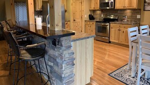 Une cuisine dotée de meubles en bois, d’un plan de travail en granit, d’une cuisinière encastrée et d’un coin bar avec des tabourets.