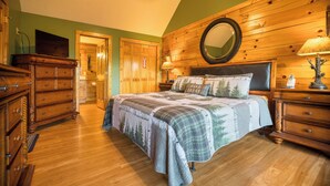 Ein Schlafzimmer mit einem hölzernen Kopfende, einem Bett mit einem zudeckenden Bettbezug zum Thema Wald, einer Holzkommode und einem Spiegel an der Wand.