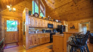 Eine Holzhütte-Küche mit Holzschränken, einer zentralen Kochinsel, Barhocker und einem großen Fenster.