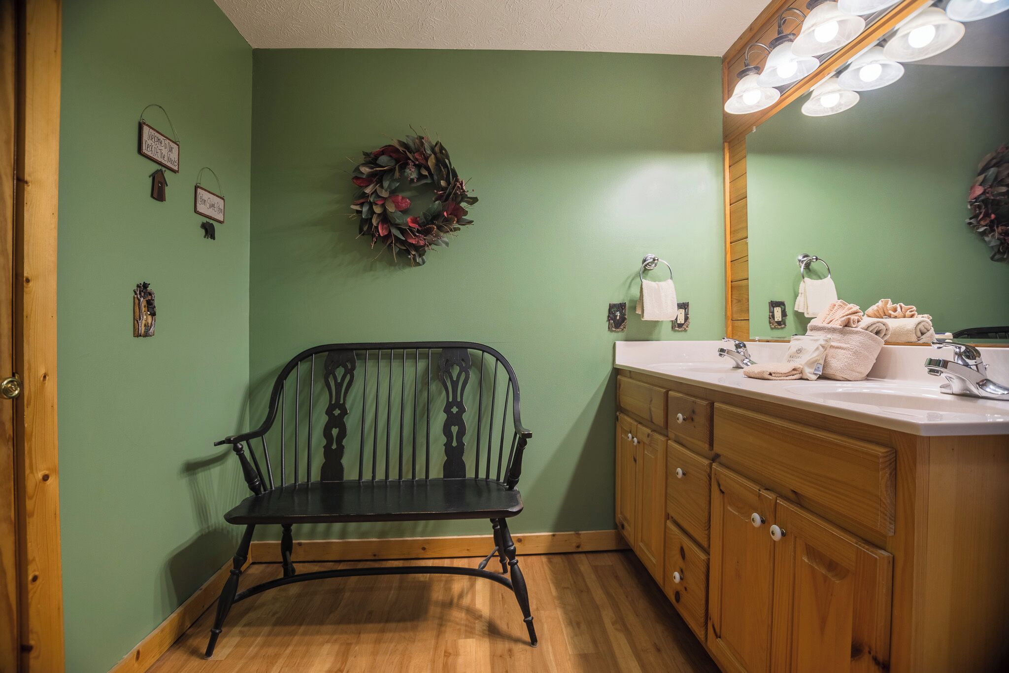 Une salle de bain avec un mur vert, un banc en bois, une commode avec un miroir et des serviettes.