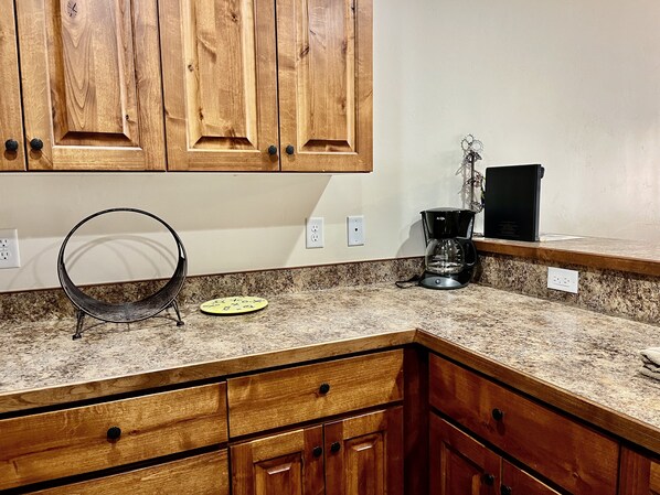 A kitchen with wooden cabinets, a granite countertop, a coffee maker, and a black metal basket.
