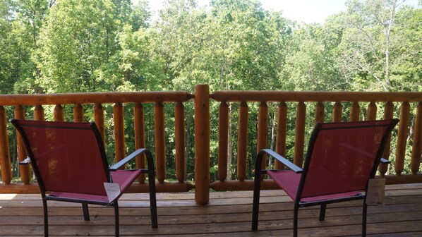 A wooden deck with two red chairs and a wooden railing.