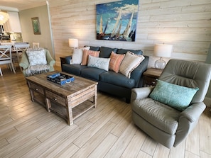 A living room with a sofa, armchair, coffee table, and a painting on the wall.