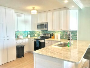 A modern kitchen with white cabinets, a microwave, a stove, and a sink.