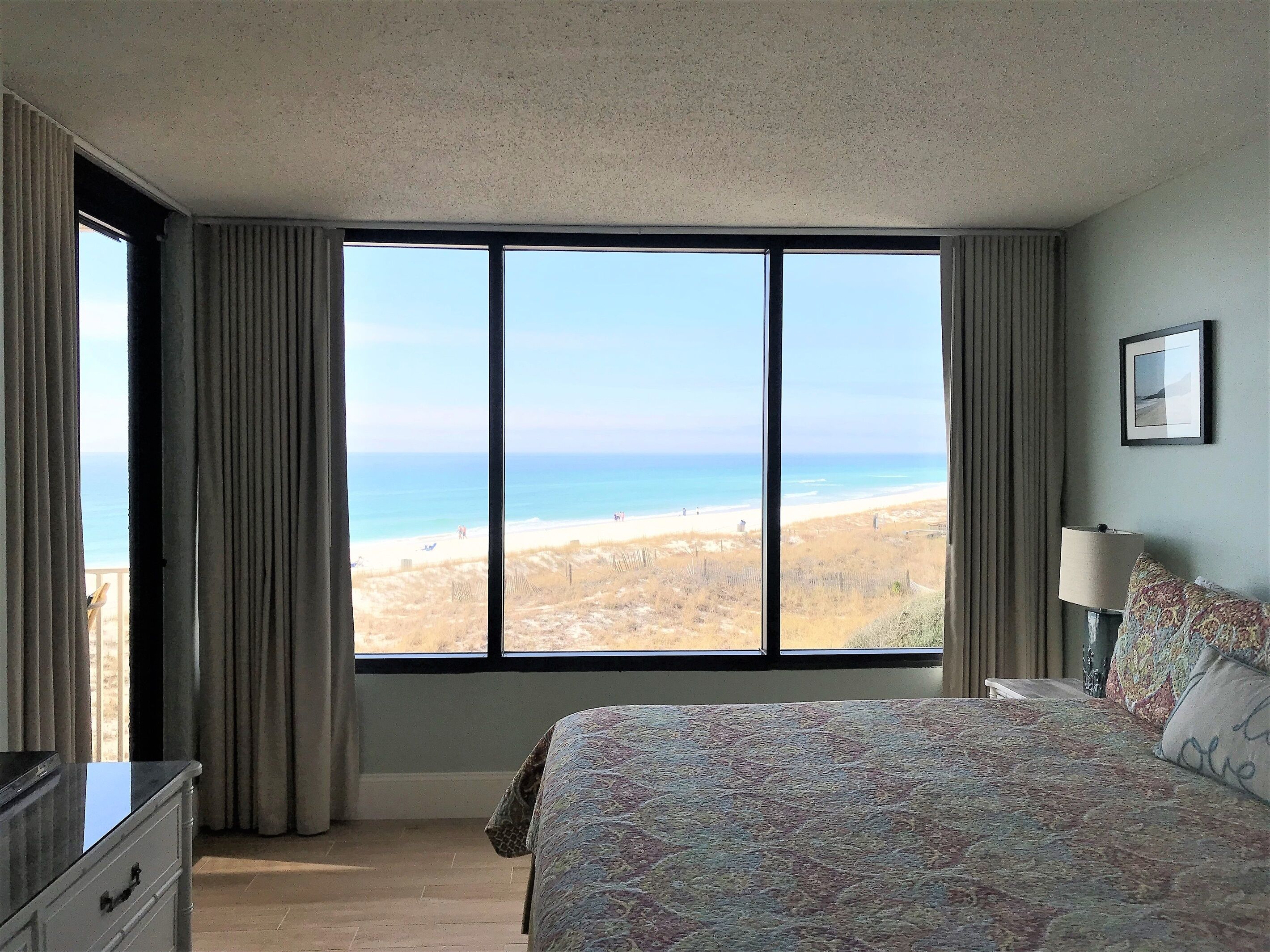 A bedroom with a large window offering a view of the beach.