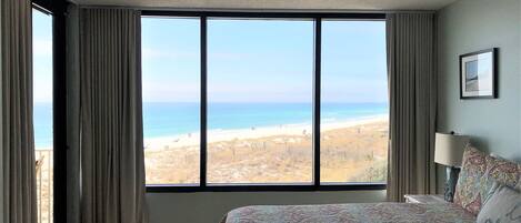 A bedroom with a large window offering a view of the beach.