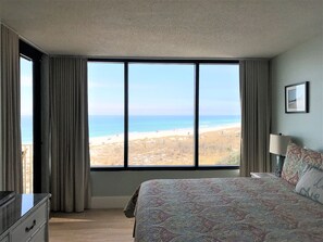 A bedroom with a large window offering a view of the beach.