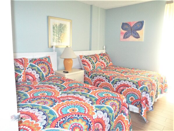 A bedroom with two beds, a nightstand with a lamp, and a framed picture on the wall.