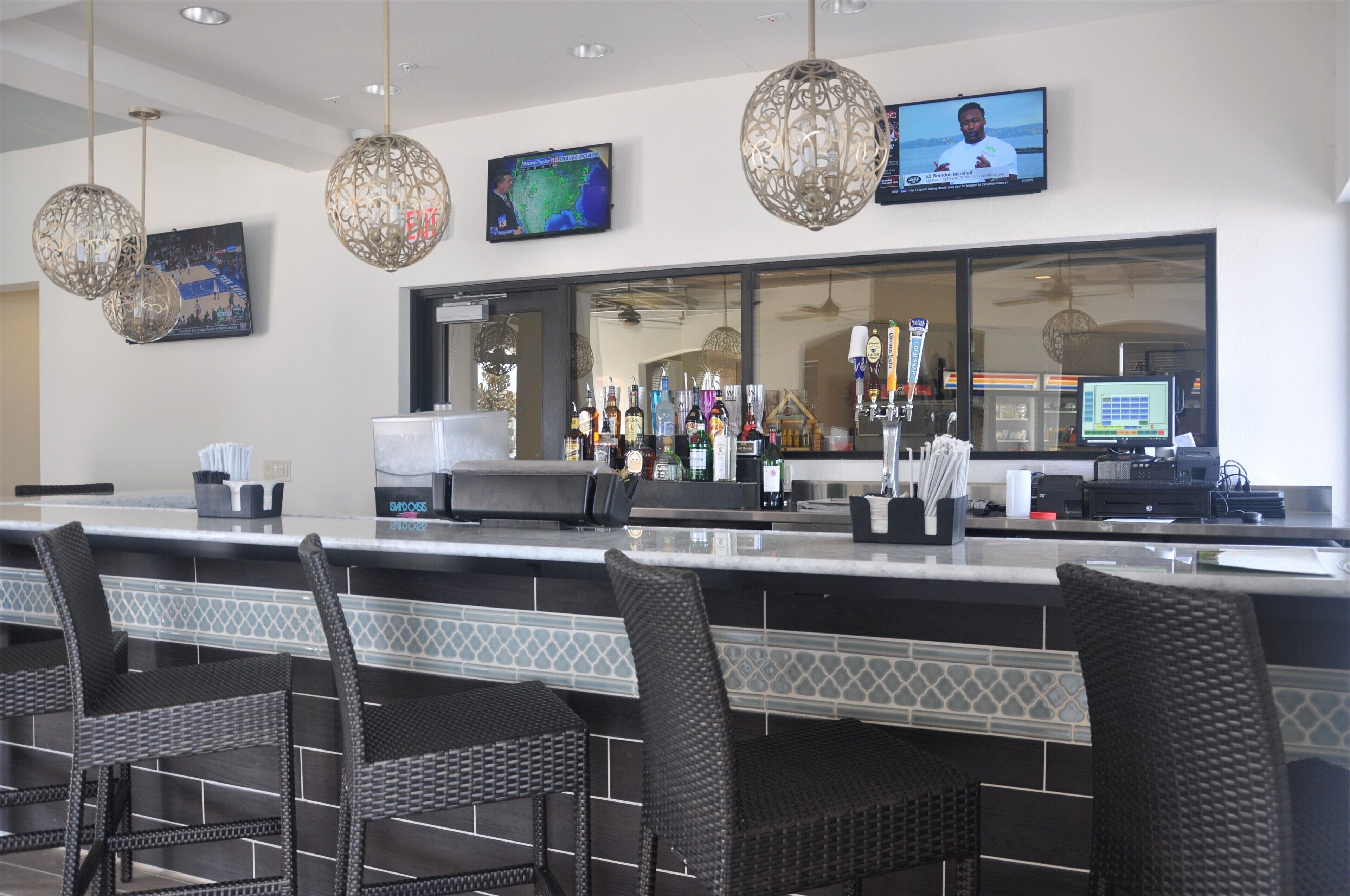 A bar area with a counter, bar stools, hanging light fixtures, a television, and a large window.