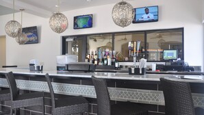 Eine Bar mit einer Theke, Barhocker, hängenden Leuchten, einem Fernseher und einem großen Fenster.
