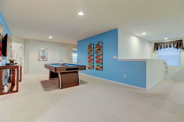 Una habitación amplia con mesa de billar, una pared azul decorativa y obras de arte.