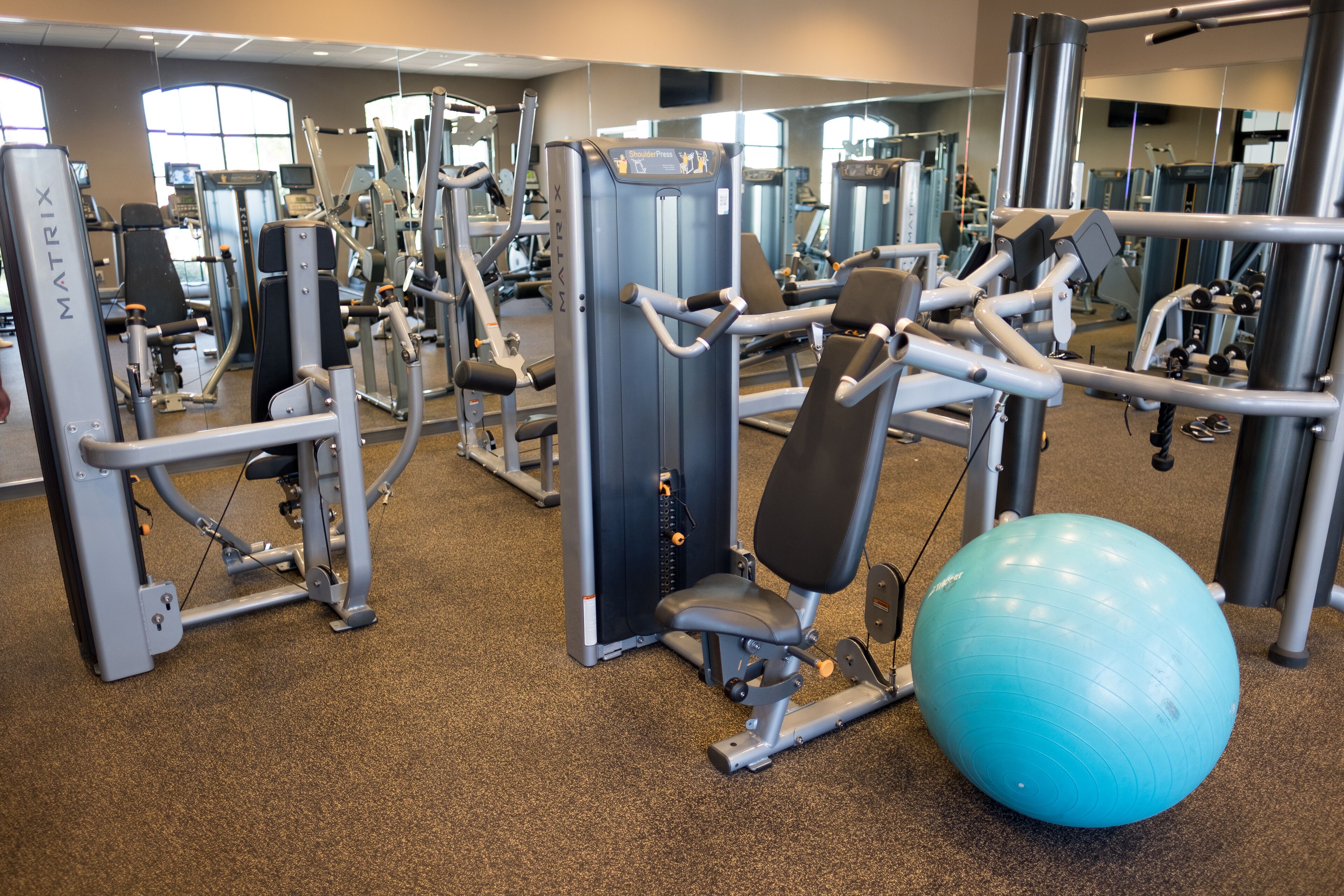 A gym with various exercise machines, a blue exercise ball, and a mirror reflecting the equipment.