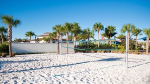 Ein Beachvolleyballfeld mit Sand, Palmen und einem Gebäude im Hintergrund.