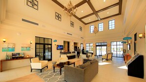 Eine großzügige Lobby mit einer Rezeption, einer Sitzecke und einer Treppe zu einer anderen Ebene.