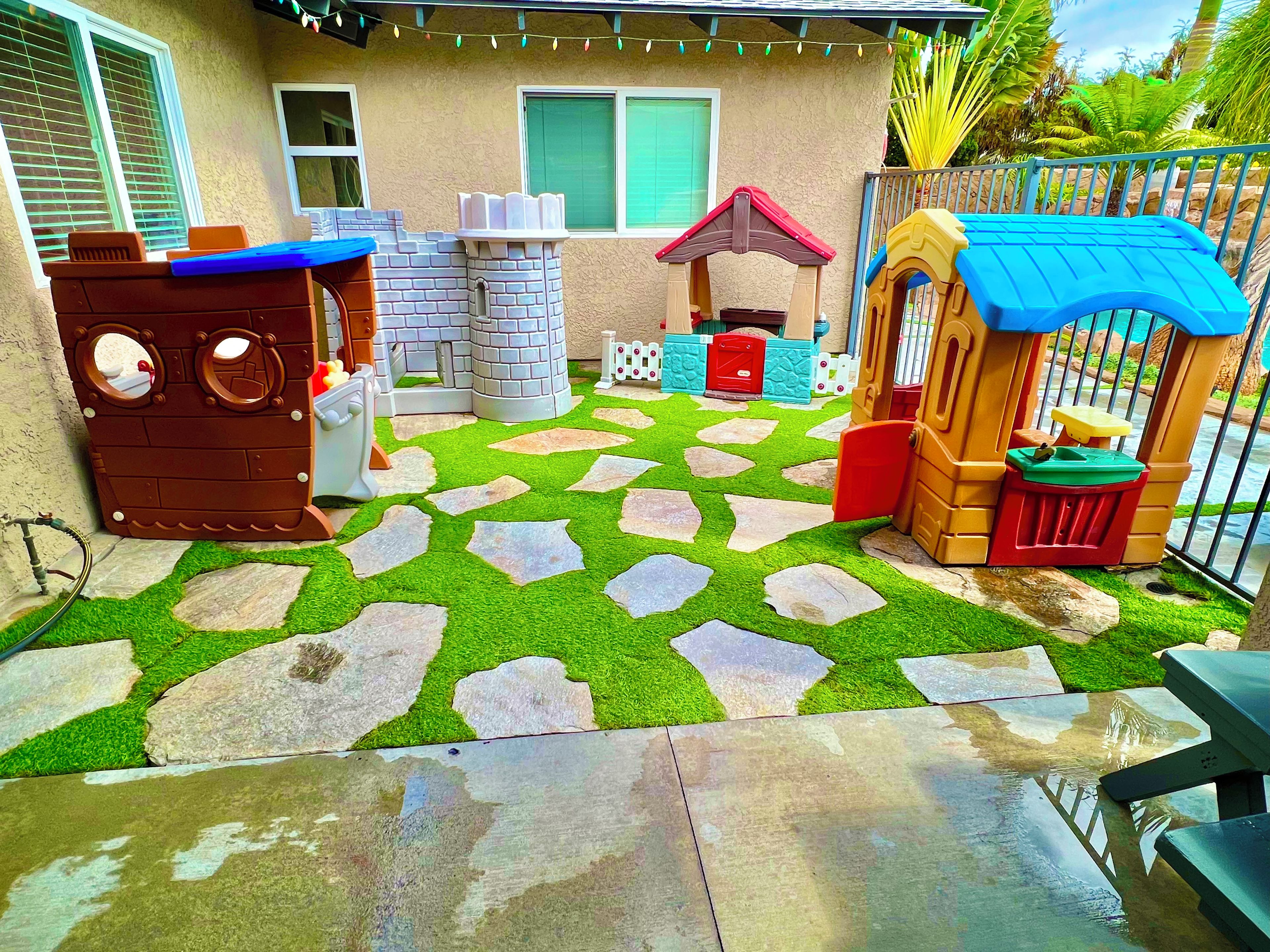 A children's play area with a brick playhouse, a small slide, and a fenced play structure.