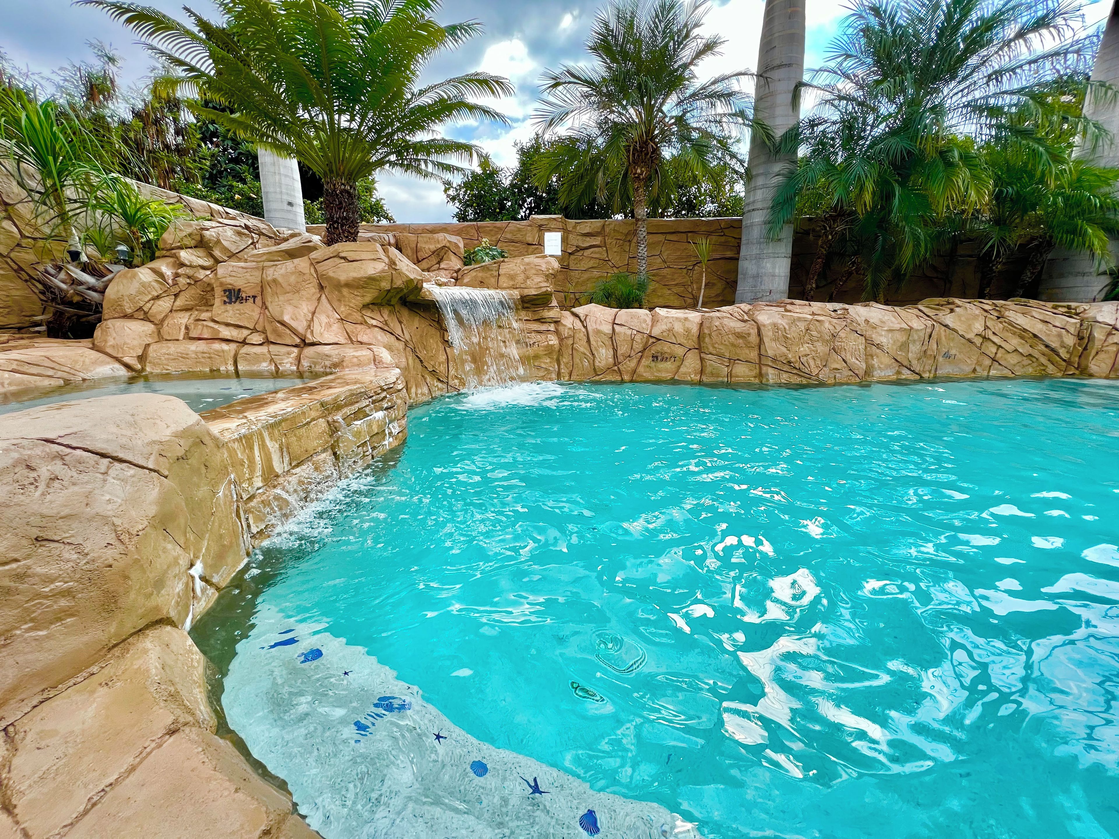 Une piscine à l’eau d’un bleu cristallin, entourée de murs rocheux et de palmiers.